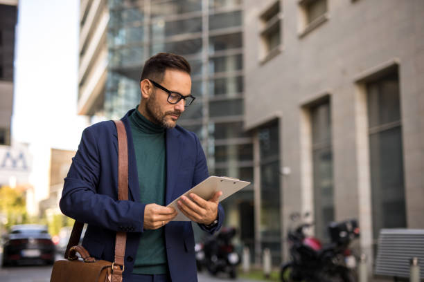 istock A handsome, smiling, well-dressed middle-aged man is going to work and holding a briefcase in his hand, with a modern building in the background. The photograph captures the fast-paced lifestyle and a business moment 2179983460