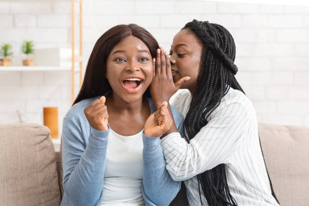 istock Two black girlfriends gossiping while sitting on sofa at home 2179984861