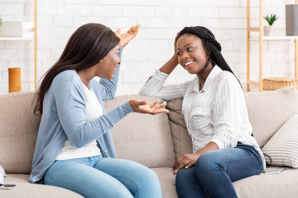 istock Two black millennial girls sitting on sofa and chatting 2179984907