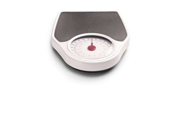 A close-up view of a mechanical bathroom scale with a measuring tape placed on top. The scale displays weight in kilograms.
