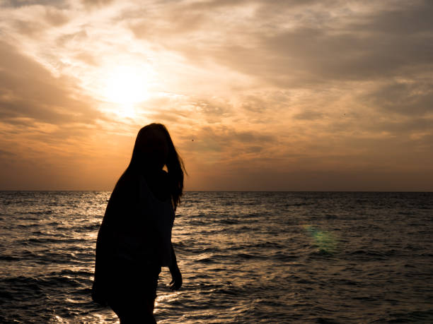 istock Woman silhouette watching sun on the beach at sunset 2179994502