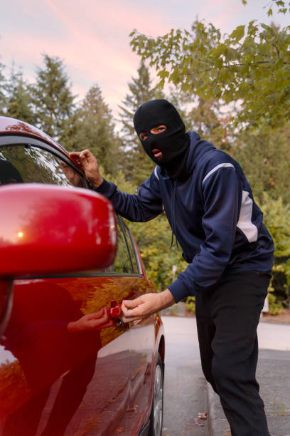 istock Masked thief breaking into a red car on the street 2179996605