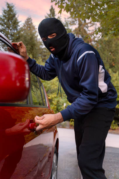 istock Masked thief breaking into a red car at dusk 2179996654