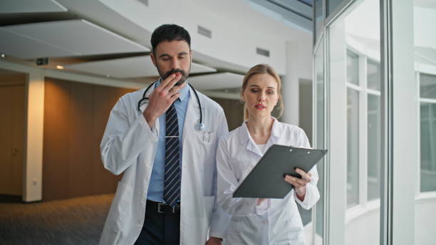 istock Physicians discussing health treatment pointing clipboard. Two doctors walking 2179999475