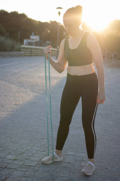 istock Young woman exercising with resistance band outdoors at sunset 2179999757