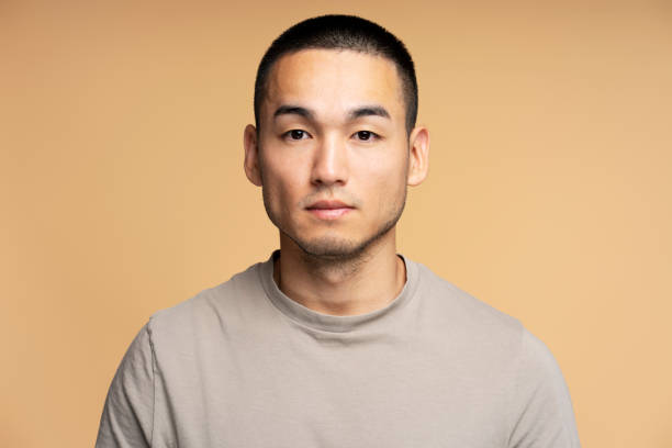 Serious young man with short hair posing on beige background
