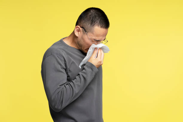 istock Sick young man blowing his nose with a tissue on yellow background 2180000376
