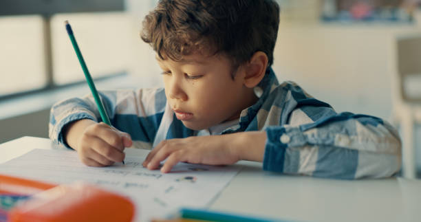istock Boy, child and writing notes in classroom for education, learning and assessment for progress at academy. Kid, quiz and activity for development, scholarship and thinking with language test at school 2180002217