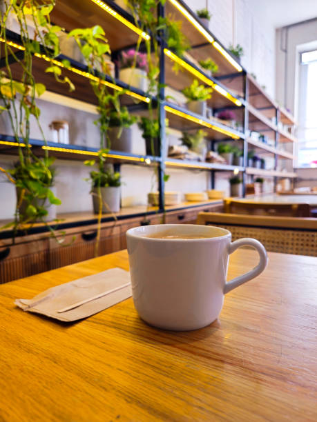 Americano coffee on a table with a recyclable napkin and wood spoon in a coffee shop with a shelf of plants in the backgroundrecyclable