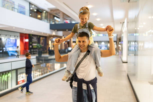 Father and daughter having fun in shopping mall Father carrying daughter on shoulders while walking through shopping mall mall walker stock pictures, royalty-free photos & images