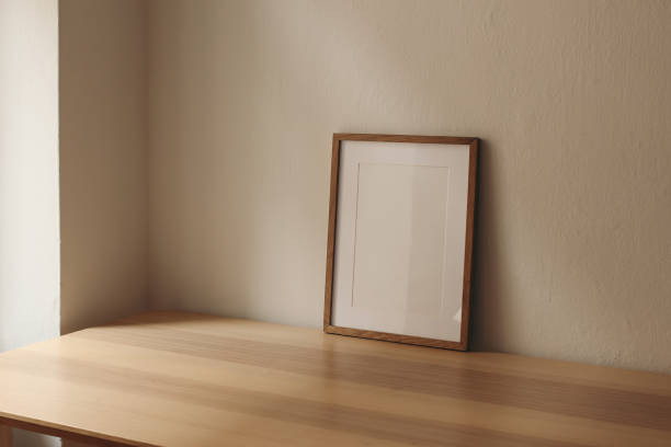 istock Vertical wooden picture frame, empty poster mockup on wooden table. No content in the frame. Beige wall background. Modern moody minimal interior decor. Side view, copy space, no people. 2180007161