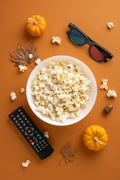 istock A cozy vertical setup with popcorn, a remote, and 3D glasses on a warm autumn background. Pumpkins and leaves add a festive touch 2180007504