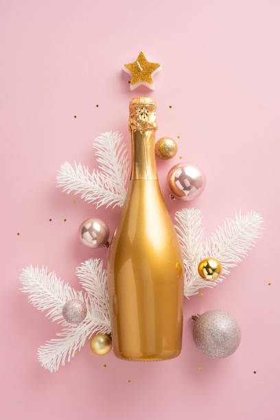 istock A gold vertical champagne bottle surrounded by festive ornaments and white branches on a pink background, symbolizing Christmas tree. Perfect for New Year or holiday themed concepts 2180007555