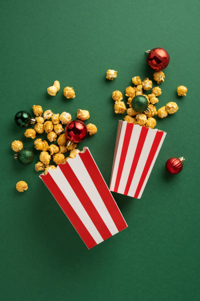 istock Vertical two red and white popcorn boxes spill delicious popcorn next to festive red and green Christmas ornaments, creating a holiday-themed snack setting 2180007590