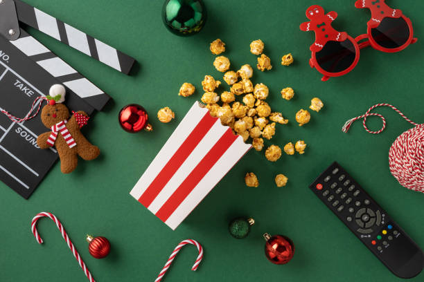 Festive Christmas themed setup featuring popcorn, holiday decorations, and a remote on a green background, capturing the essence of a cozy movie night during the holiday season