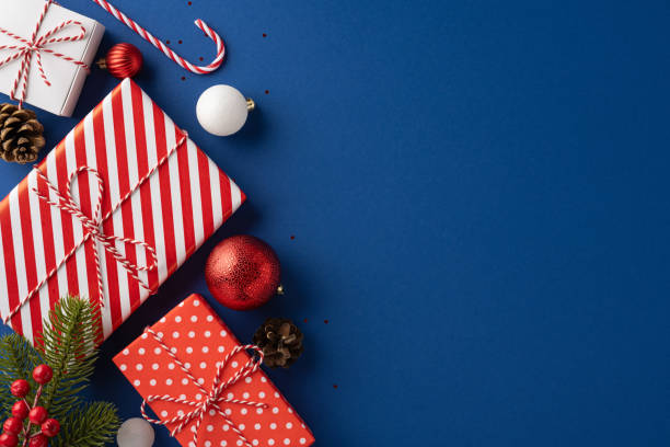 istock Top-down view of Christmas presents and decorations on a blue background, featuring red and white patterns, pine cones, and baubles 2180007661