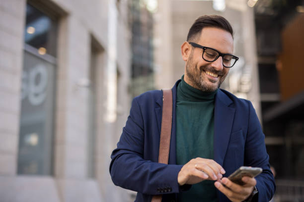 istock A handsome, well-dressed business man stands in front of a modern building, using his phone to write a business email. It’s morning, and he is engaged in work obligations while enjoying the beautiful day and feeling positive. 2180014898