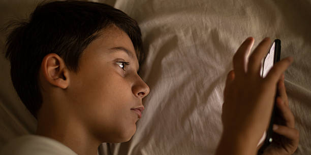 istock boy with mobile phone in bed touching the screen 2180019007