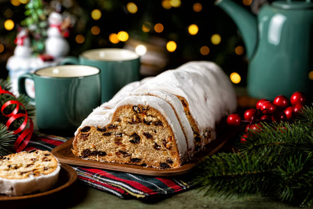 istock Served table with Stollen cake, tea cups and pot. German Christmas dessert, bread chock full of dried fruit, candied peel, and almonds. Festive lights and decoration. 2180021693
