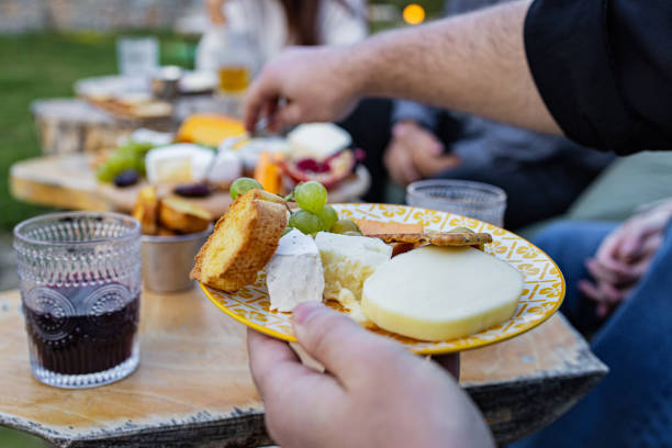 Friends enjoying beautiful cheese arrangement on a table, outdoors at a picnic area.