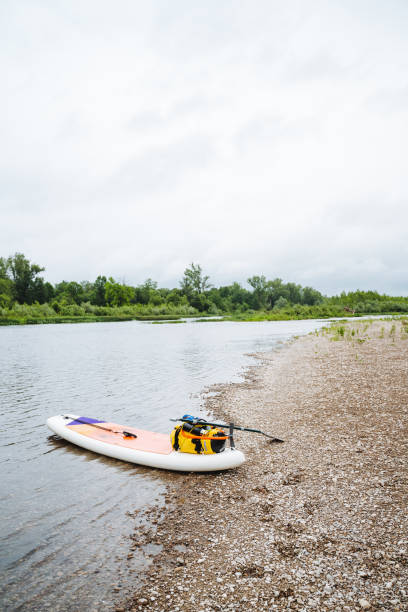 istock A paddle board rests on the riverbank under the open sky. It represents tranquility and adventure, a perfect blend of nature and watercraft, providing a serene scene by the water 2180044499