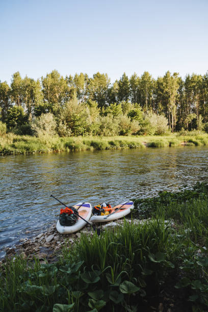 istock Two kayaks are peacefully lying on the riverbank under a clear sky, surrounded by trees and serene water. This tranquil scene reflects a sense of calmness and harmony with nature 2180044564