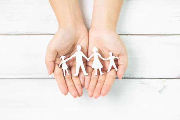 istock Family Unity: Hands Gently Holding Paper Family Silhouettes on White Background 2180049849