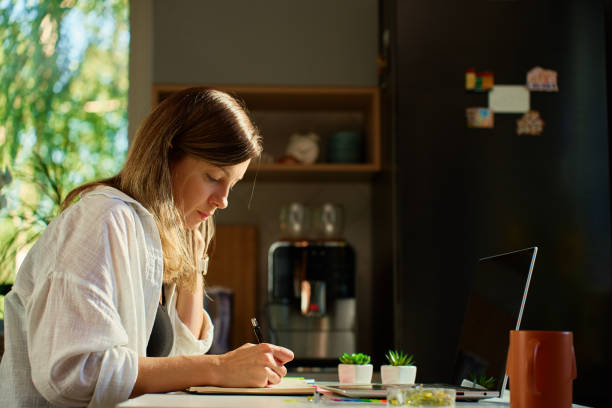 istock Woman working at home, writing in notebook and using laptop 2180050970