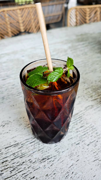 Refreshing iced black tea with mint garnish in a textured glass featuring a paper straw on a rustic outdoor cafe table setting for a relaxing beverage break