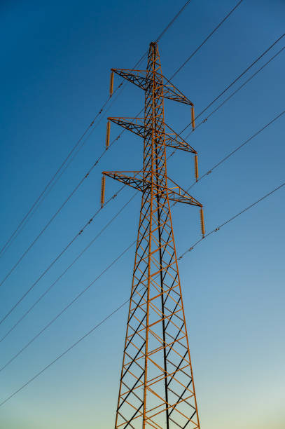 This is a shot of a high-voltage electric transmission tower, also known as an electricity overhead line pylon or lines, at sunset