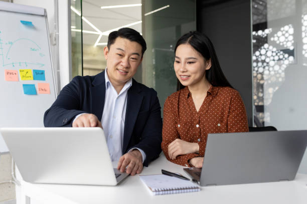 istock Asian business team collaborating on project using laptops and discussing ideas in modern office setting with charts and notes. 2180056940