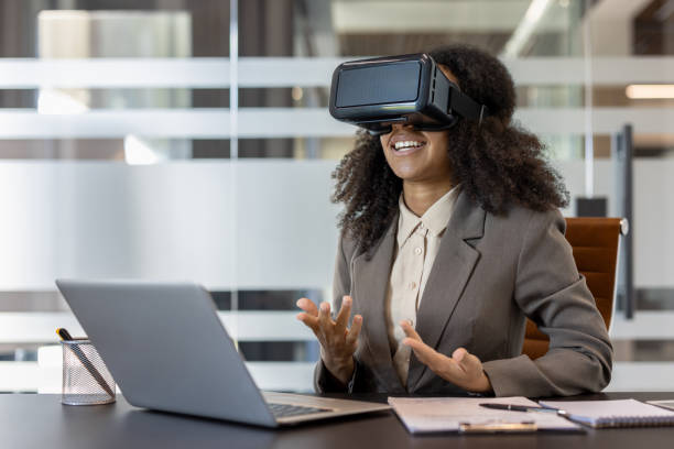 istock Business professional experiencing virtual reality through VR headset while working at laptop in modern office setting 2180060099