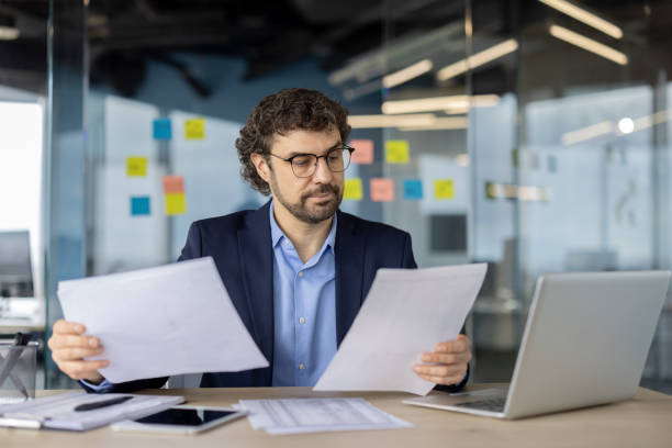istock Mature financier examining paperwork in modern office environment with natural lighting and glass walls, emphasizing professionalism. 2180066940