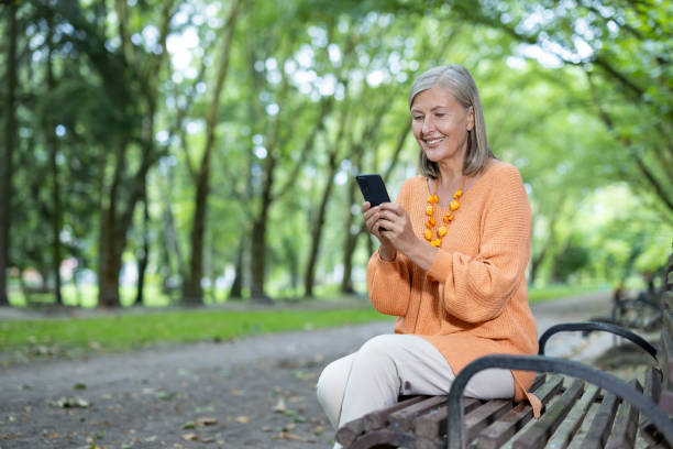 istock Senior woman smiling while using smartphone on park bench on a sunny day, enjoying leisure and staying connected outdoors 2180070668