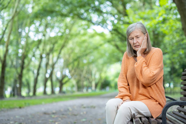 istock Senior woman experiencing toothache while sitting on a bench in a park and holding her face in discomfort 2180070749