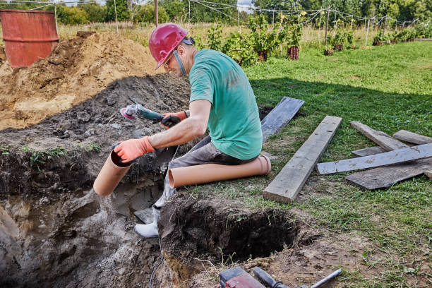 istock Plumber cuts off section of plastic sewer pipe during installation of an autonomous sewerage system in rural area. 2180073211