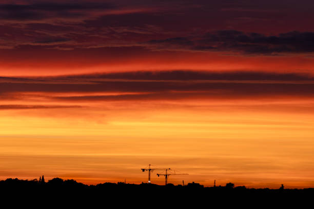 A stunning sunset illuminates vibrant colors across a city skyline, with construction cranes silhouetted against it