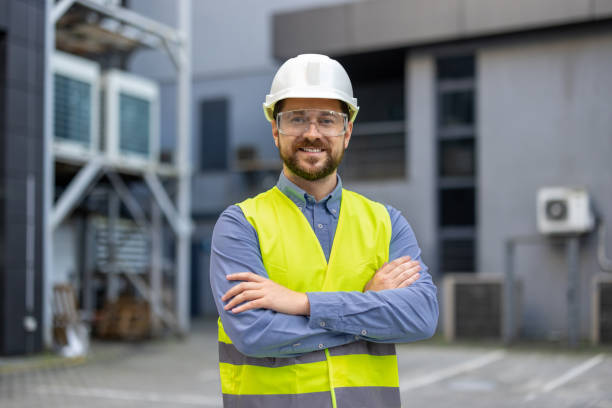 istock Confident construction worker wearing safety vest and helmet smiling while standing at an industrial site, showcasing professionalism and readiness in engineering field 2180074444