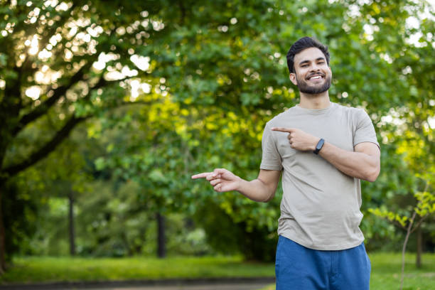 istock Smiling man pointing in park, wearing smartwatch, under sunlight creating a cheerful atmosphere 2180076760