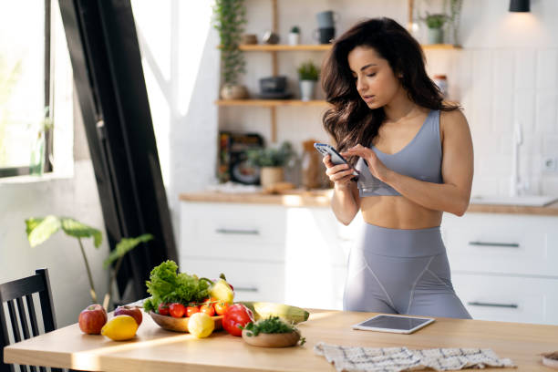 istock Young woman wearing sportswear using smartphone in kitchen with fresh vegetables on table 2180079473