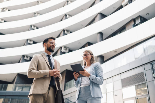 istock Business partners discussing project using tablet in front of modern office building 2180092707