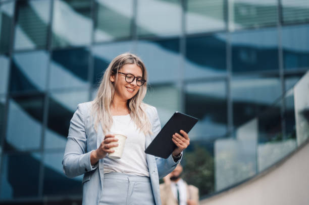 istock Smiling businesswoman using digital tablet and holding coffee outside office building 2180092716