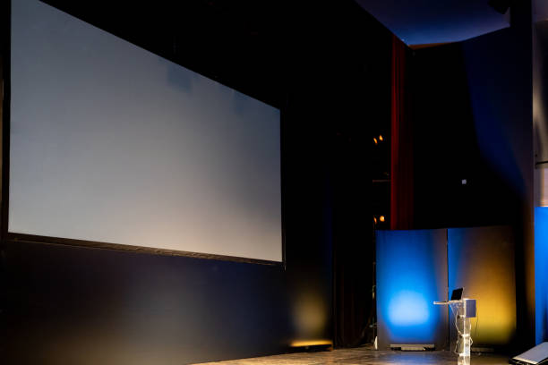 istock Presentation setup with an empty screen and a laptop on stage in a dimly lit auditorium before a conference begins 2180093120