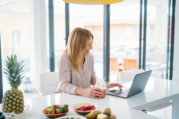 istock Woman Working on Laptop with Smoothie in Bright Kitchen 2180097939
