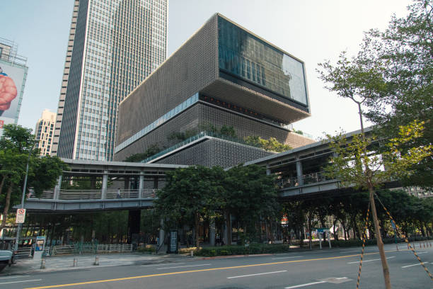 The city of Taipei showcases a striking modern building surrounded by greenery and bustling streets, highlighting the blend of nature and urban life. The clear sky adds to the vibrant atmosphere.