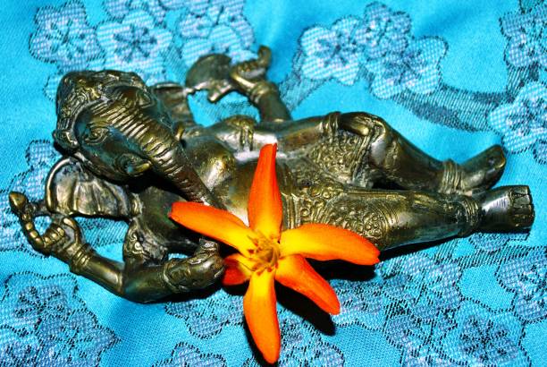 bowl with bougainvilleas and incense sticks and a statuette of god Ganesha blurred in the background