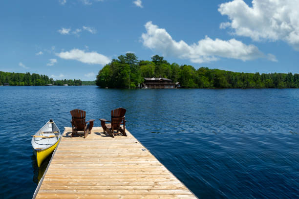 istock Two cottage Adirondack chairs on a dock overlook the lake. 2180101862