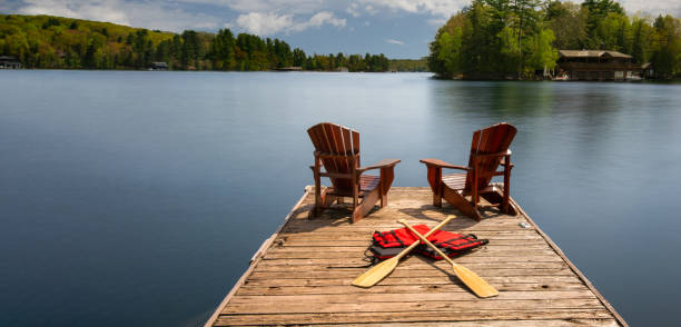 istock Two Adirondack chairs on a dock with canoe paddles and life jackets 2180101865