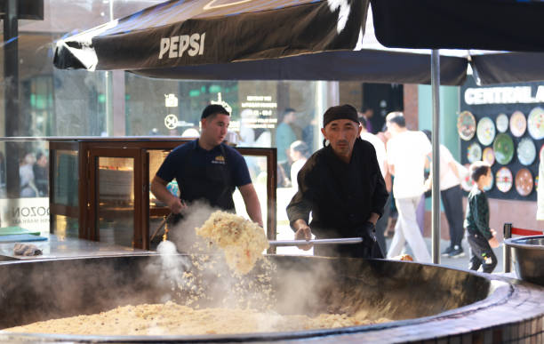Tashkent, Uzbekistan - September 29 2024: chef fired the plov or pilau in kitchen in a bigh cauldron. Plov is one of famous food in Central Asia which recipe usually involves cooking in stock or broth, adding spices