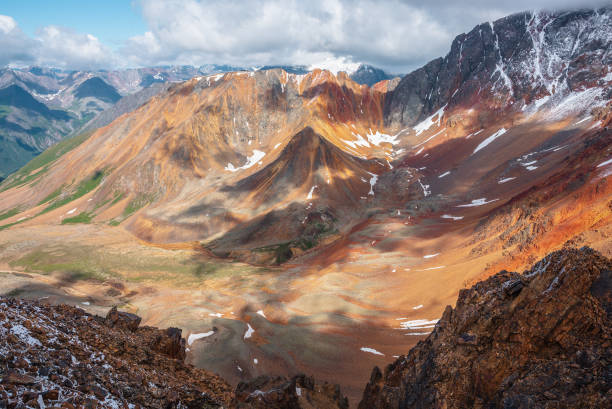 istock Top view from rock abyss edge to rounded multicolor valley with curved iron river and big sharp rocky ridge of red color. Colorful large mountains. Rocks in freshly fallen snow. Vivid alpine scenery. 2180109757
